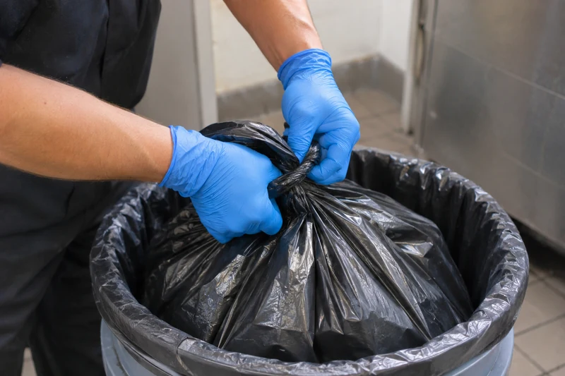 Gloved hands sealing a trash bag inside a second bag